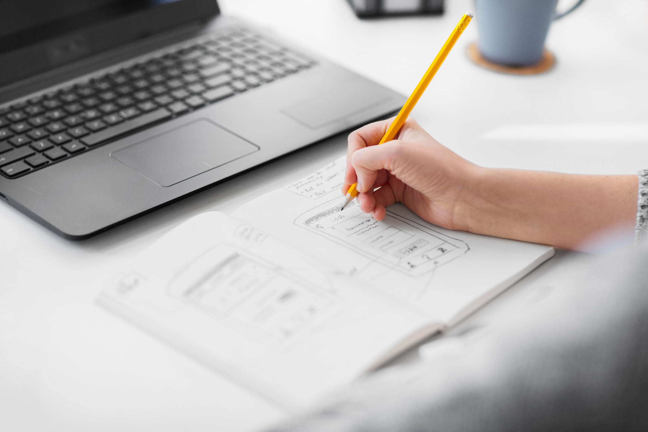 Designer sketching website layout on paper and laptop